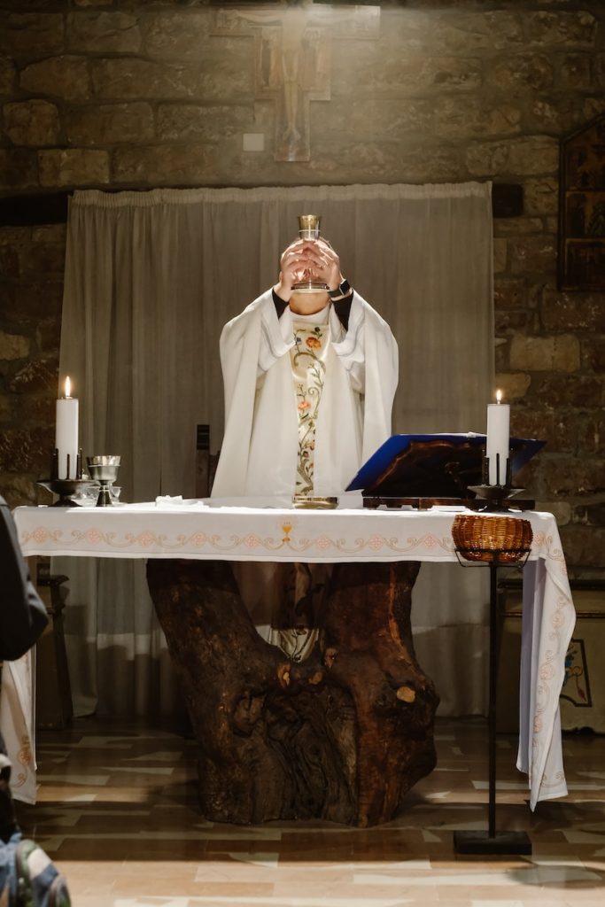 priest lifting goblet while standing beside table